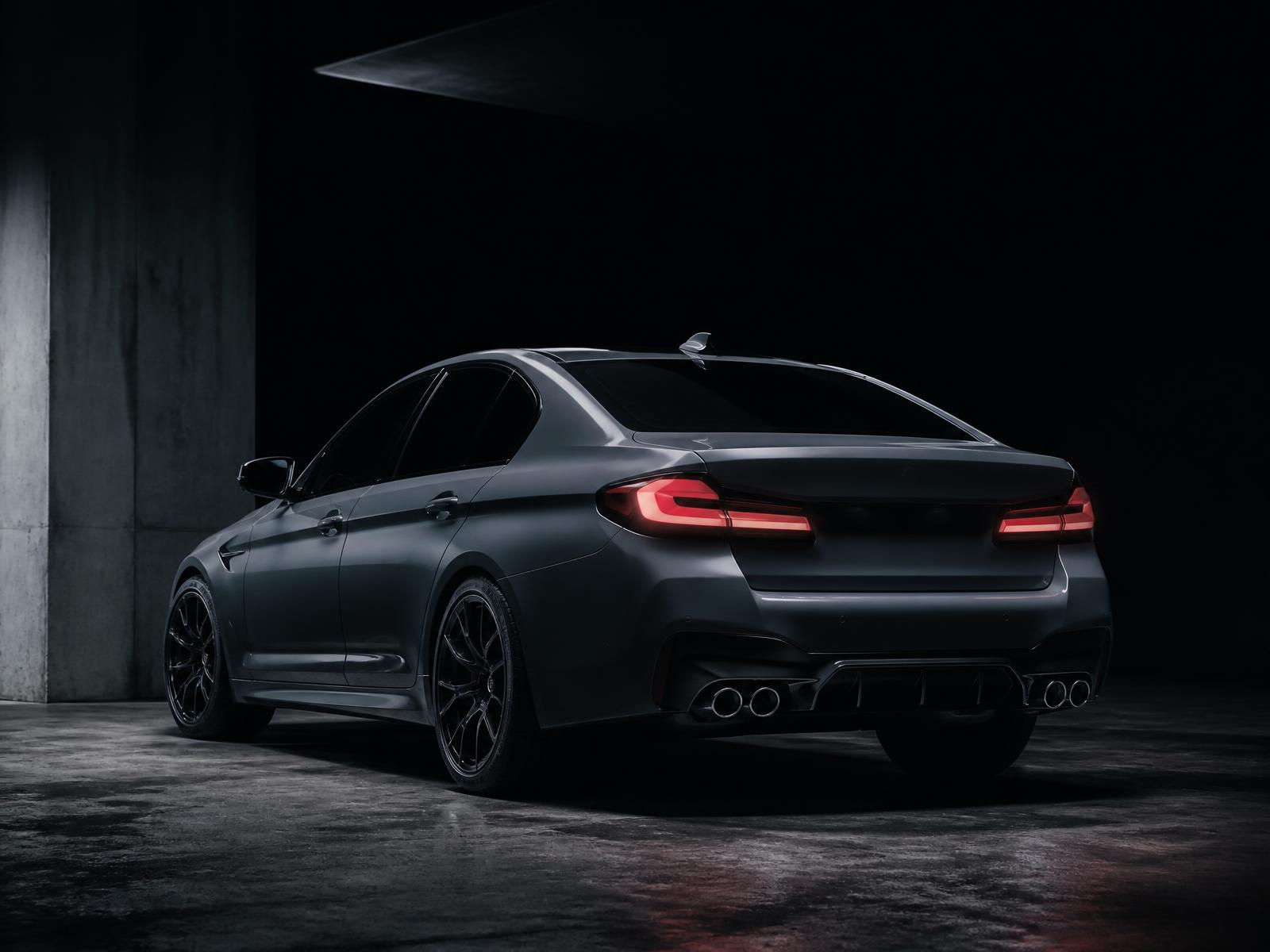 Dark studio photograph of a modern BMW sedan rear three-quarter view